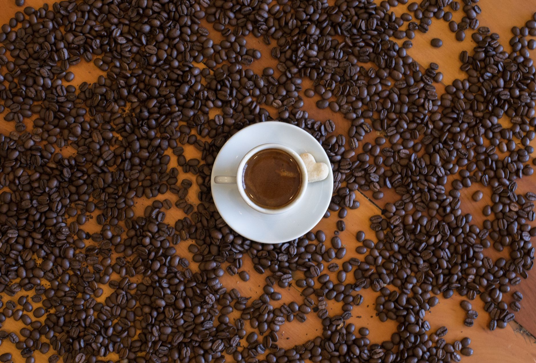Whole dark-roast coffee beans spilling from a bag onto a wooden table