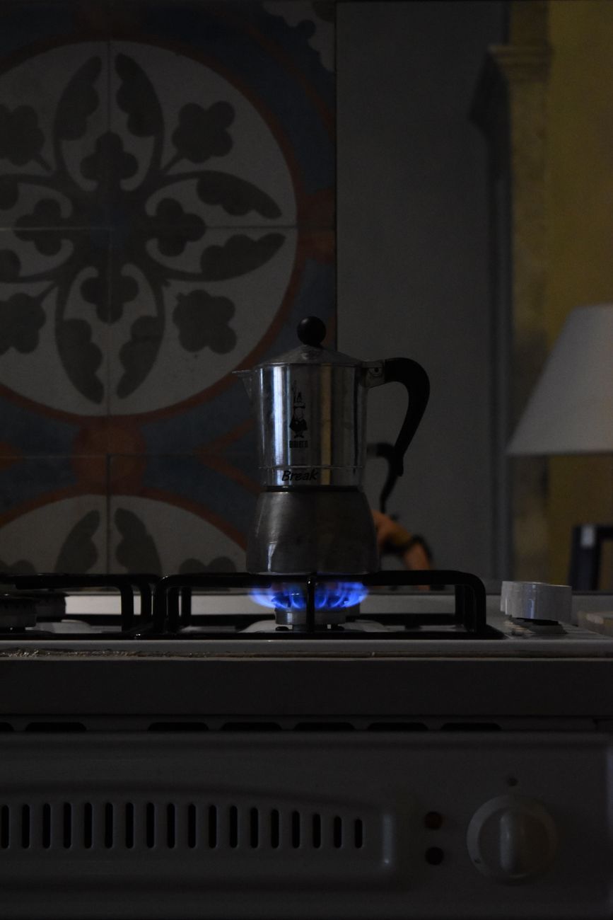 A moka pot brewing coffee on a lit gas stove